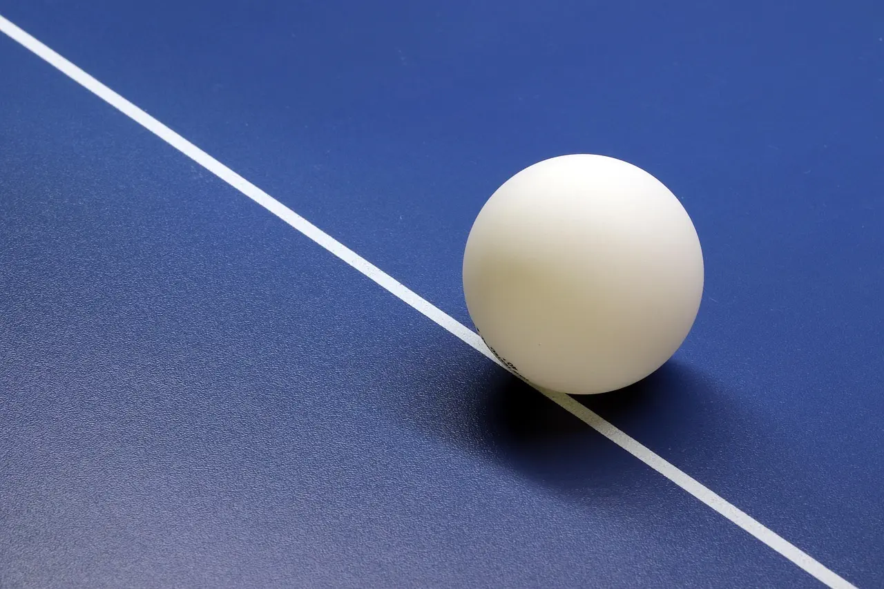 Hvid bordtennisbold på blåt bord med hvid linje